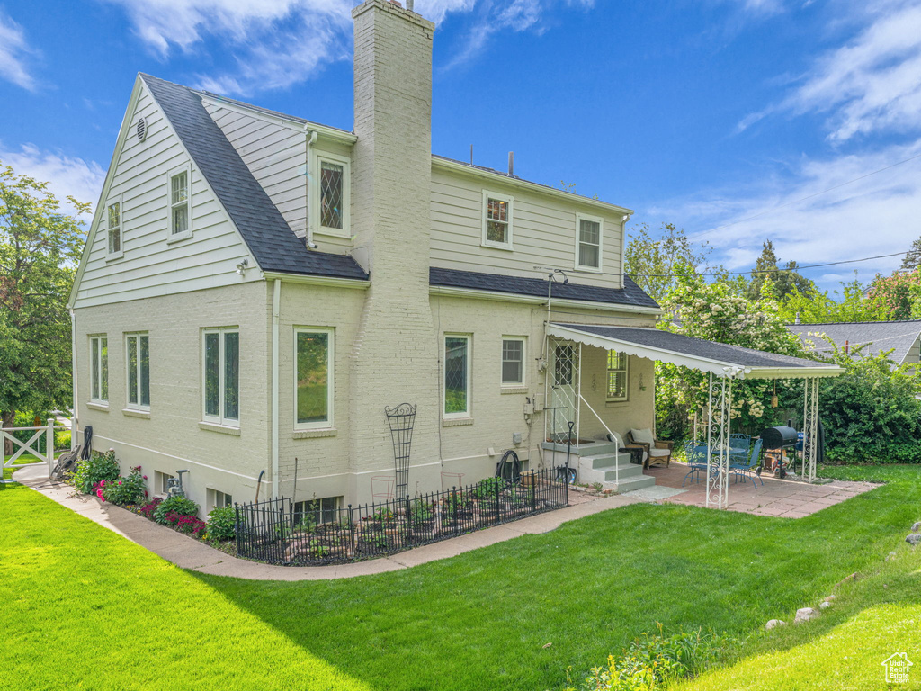 Rear view of house featuring entry steps, a chimney, a patio area, roof with shingles, and brick siding