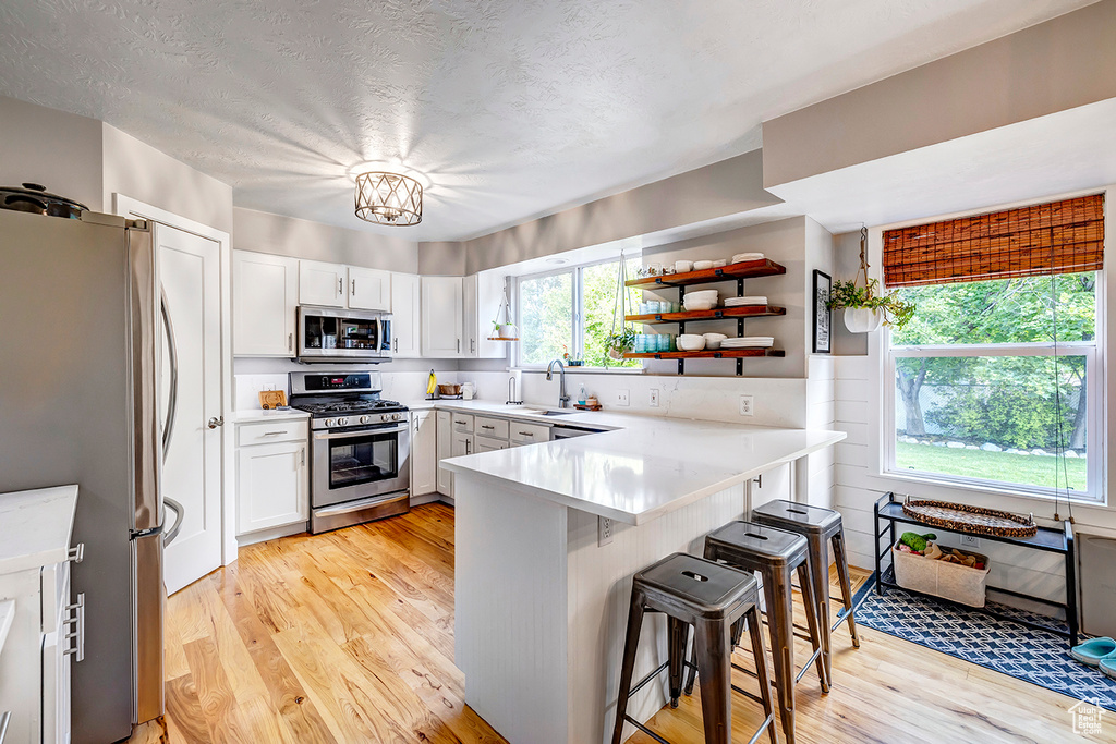 Kitchen featuring stainless steel appliances, a peninsula, healthy amount of natural light, light wood-type flooring, and a textured ceiling