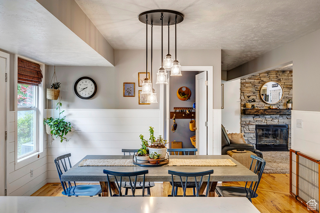 Dining room with wood finished floors, a fireplace, a wainscoted wall, and a textured ceiling