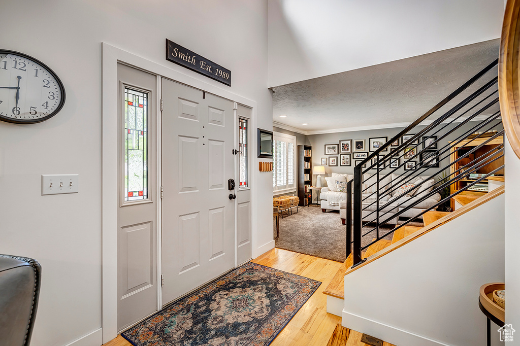 Foyer entrance with plenty of natural light, crown molding, light wood-style flooring, stairs, and baseboards