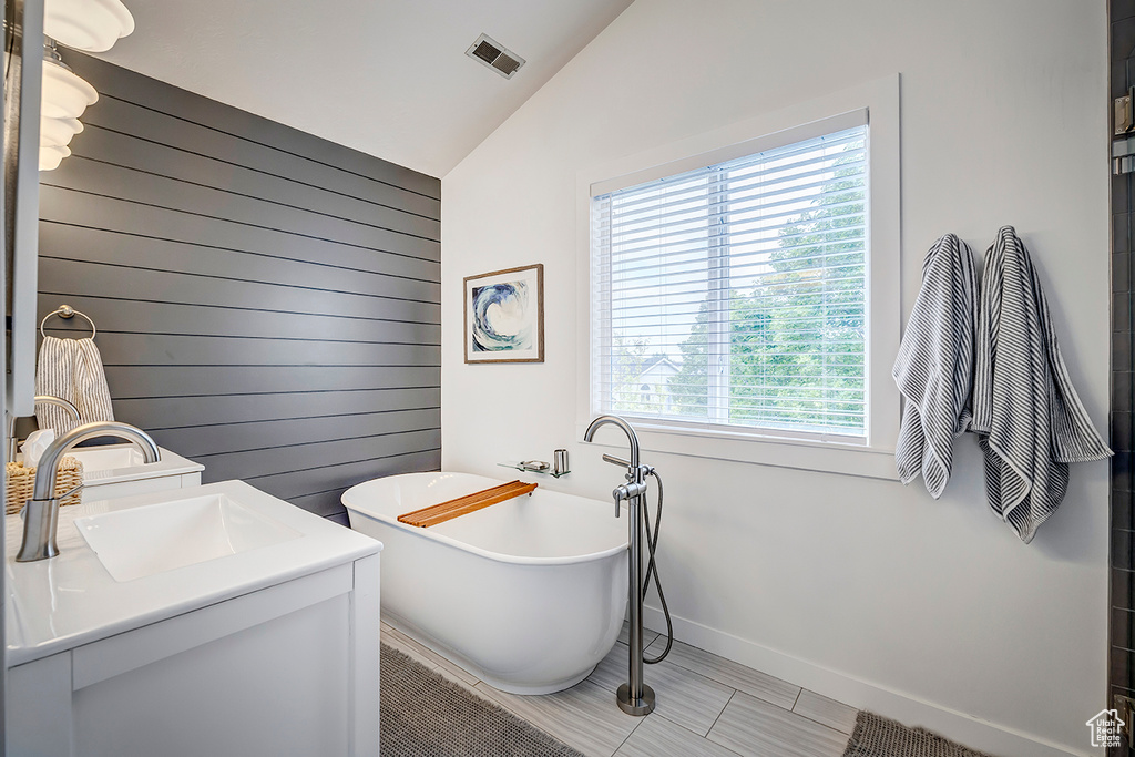 Bathroom featuring vaulted ceiling, wooden walls, a freestanding tub, vanity, and baseboards