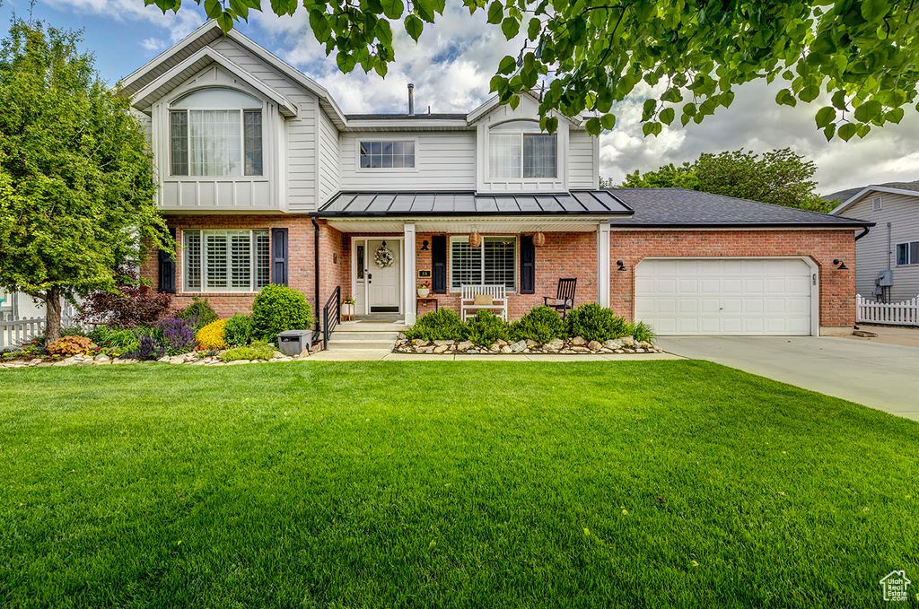 View of front facade with brick siding, covered porch, an attached garage, and driveway