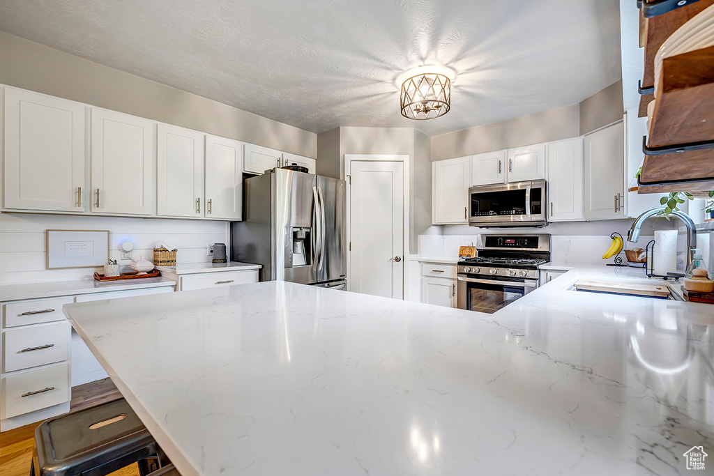 Kitchen featuring stainless steel appliances, a sink, light stone counters, white cabinetry, and a peninsula