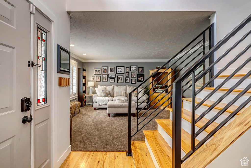 Entryway with ornamental molding, light wood-style flooring, stairs, baseboards, and a textured ceiling