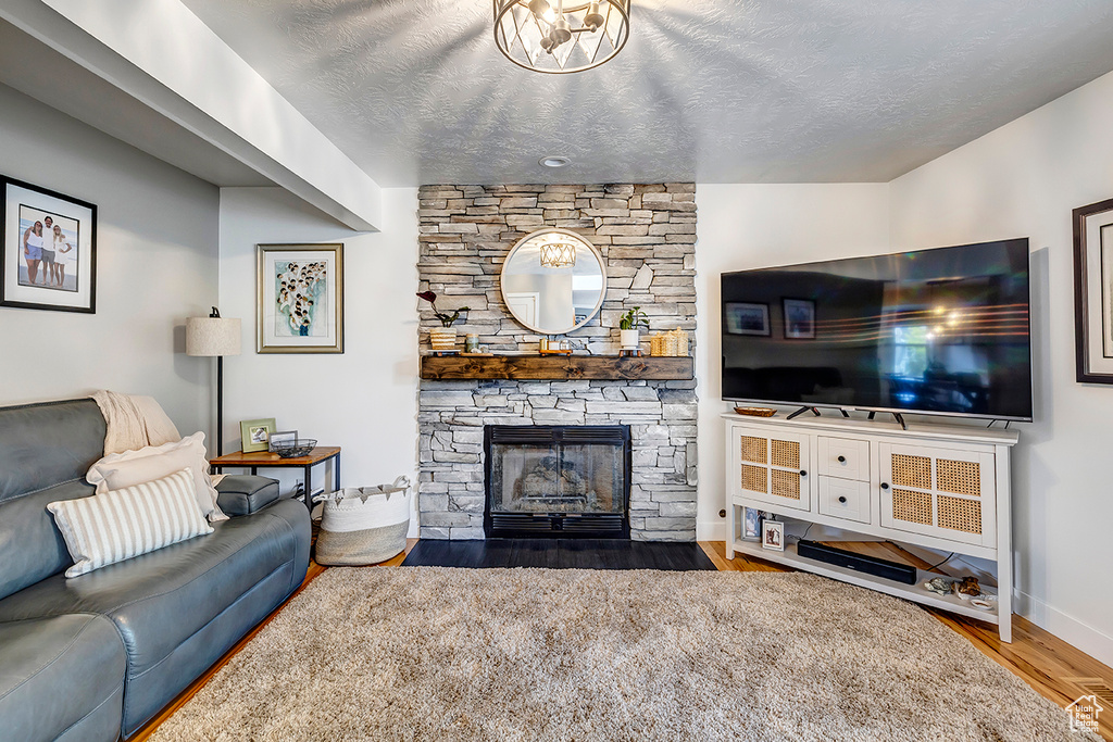 Living room featuring wood finished floors, a stone fireplace, baseboards, and a textured ceiling