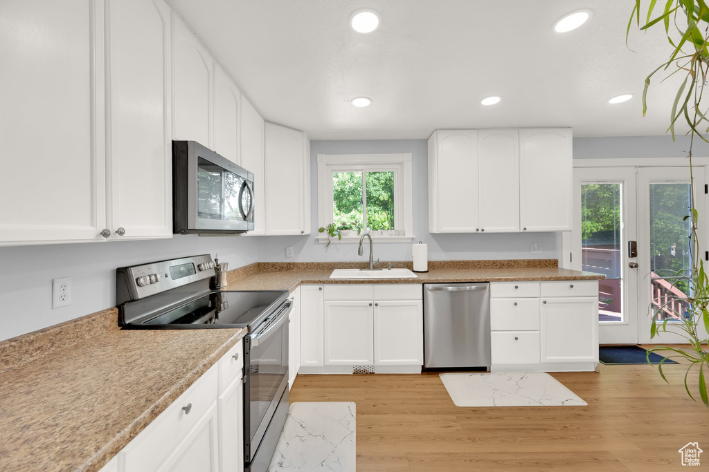 Kitchen with appliances with stainless steel finishes, a sink, white cabinets, light wood-style flooring, and recessed lighting
