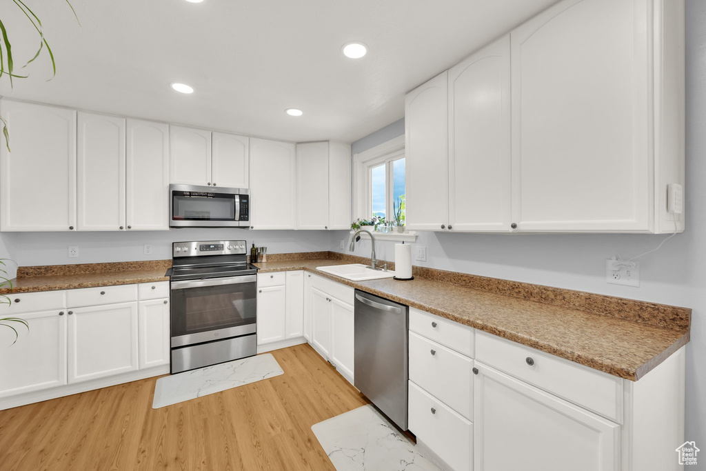 Kitchen with stainless steel appliances, a sink, light wood-style flooring, recessed lighting, and white cabinetry
