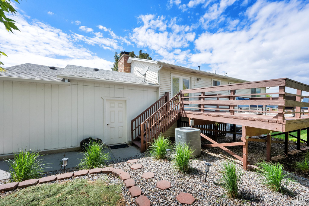 Rear view of house with a wooden deck, stairs, a chimney, and central AC unit