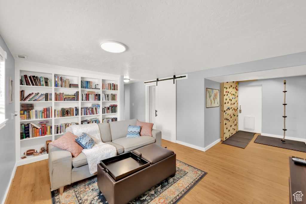 Living room with a barn door, wood finished floors, baseboards, and a textured ceiling
