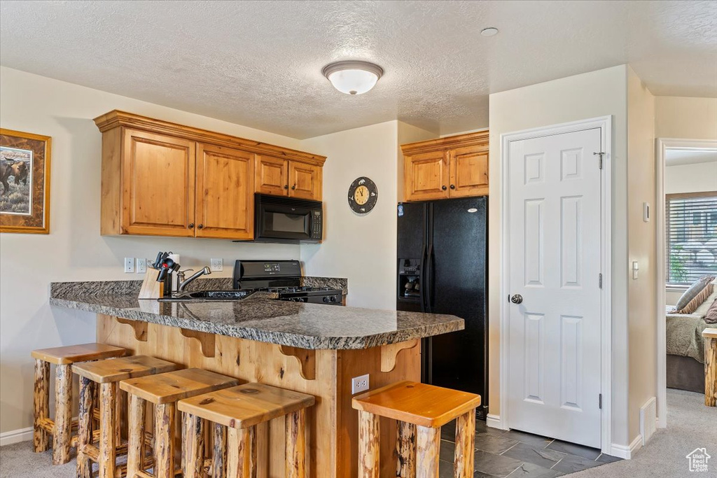Kitchen with black appliances, a sink, a kitchen breakfast bar, baseboards, and a peninsula