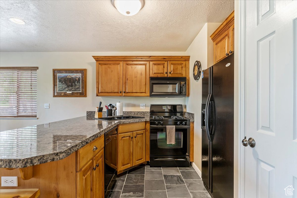 Kitchen featuring black appliances, a peninsula, dark countertops, brown cabinets, and a textured ceiling