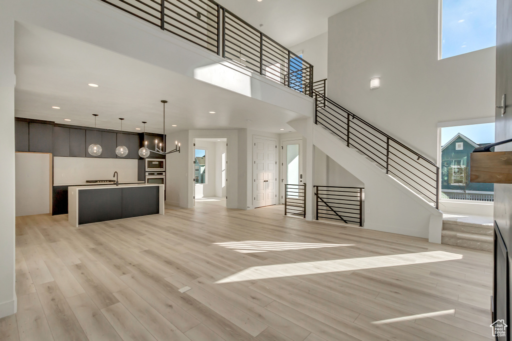 Unfurnished living room with a towering ceiling, light wood-style flooring, healthy amount of natural light, a chandelier, and recessed lighting