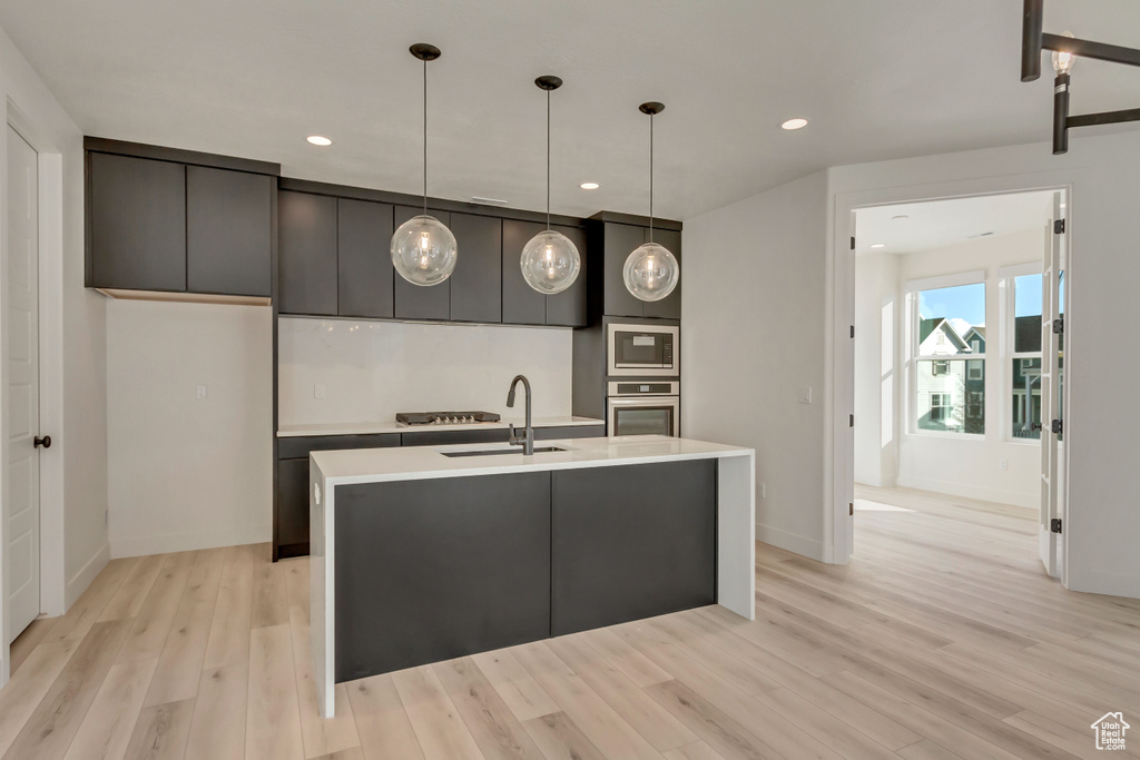Kitchen featuring appliances with stainless steel finishes, a sink, light wood-style floors, light countertops, and hanging light fixtures