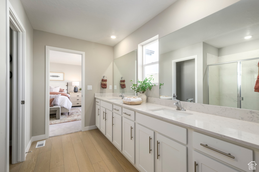 Full bathroom featuring wood finished floors, a shower stall, double vanity, connected bathroom, and baseboards