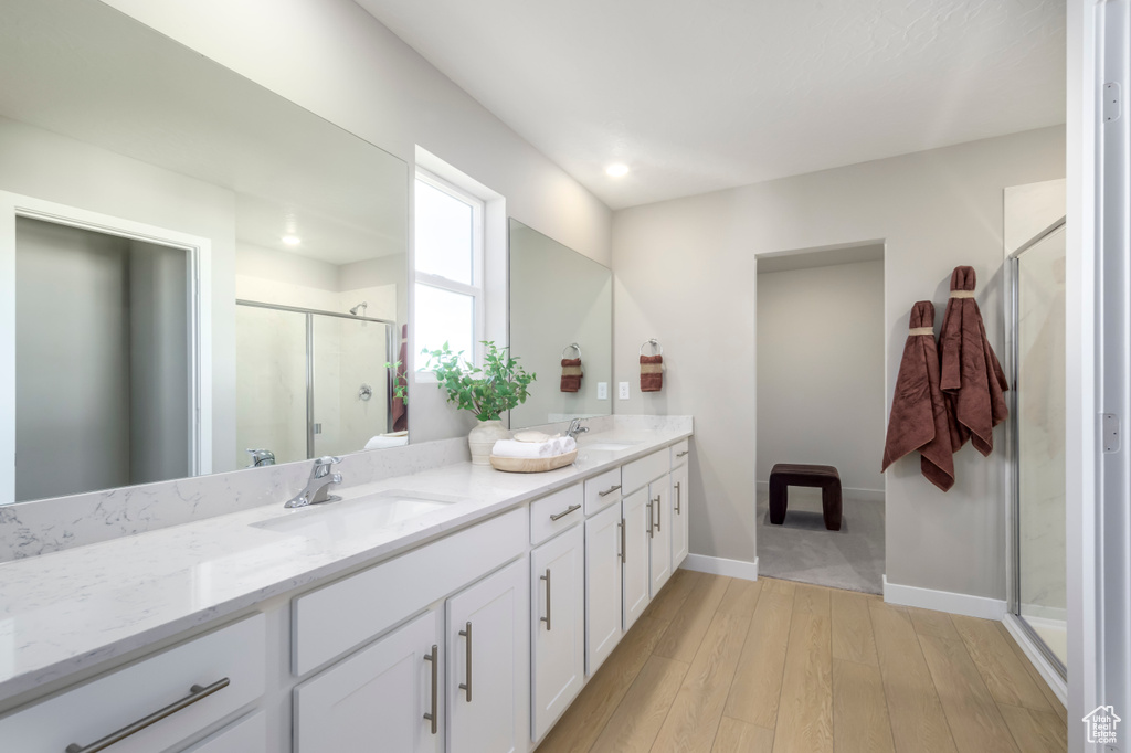 Full bathroom with double vanity, wood-type flooring, a shower stall, baseboards, and recessed lighting