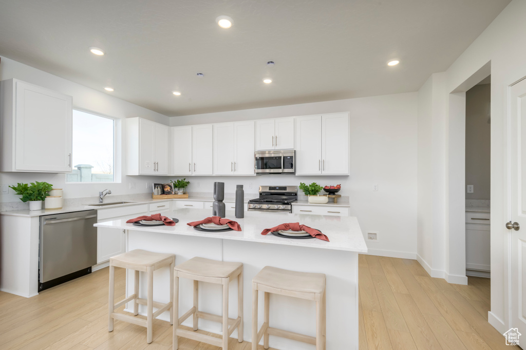 Kitchen featuring stainless steel appliances, light countertops, a breakfast bar area, light wood-type flooring, and recessed lighting