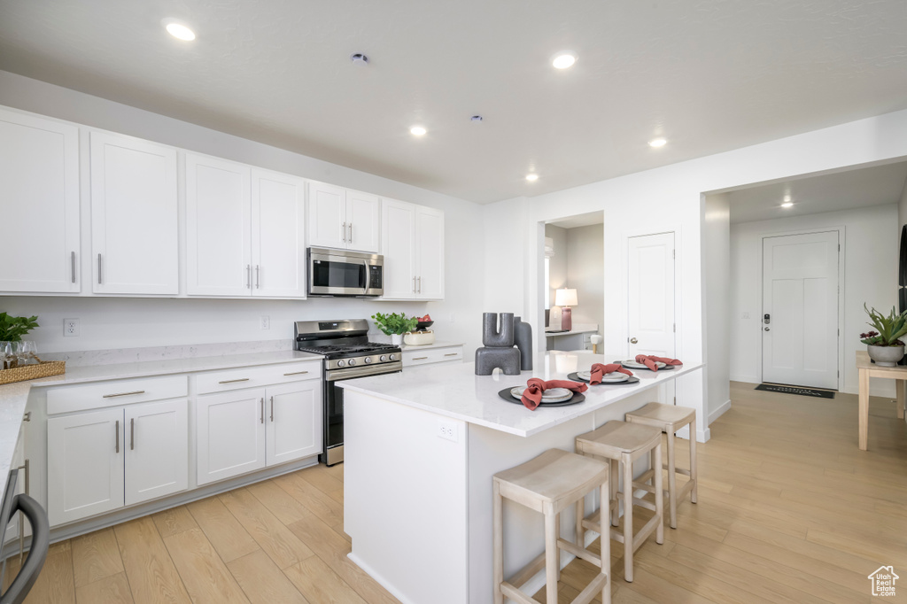 Kitchen featuring appliances with stainless steel finishes, light wood-style flooring, white cabinetry, a breakfast bar, and recessed lighting