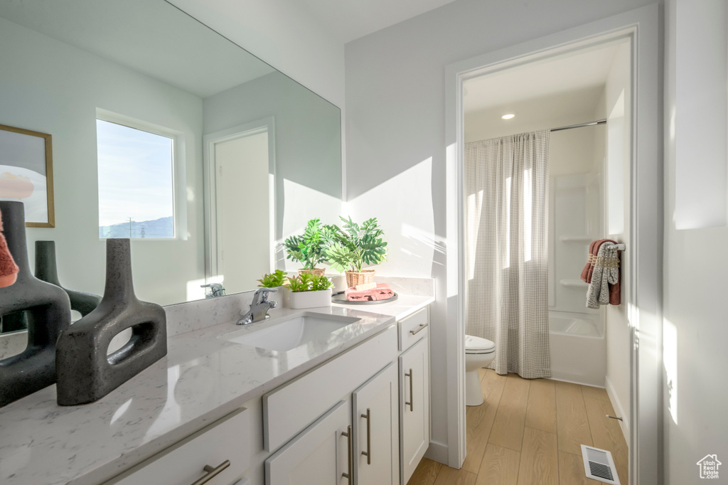 Bathroom featuring toilet, wood finished floors, vanity, and shower / bath combo with shower curtain