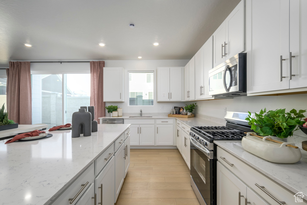 Kitchen featuring appliances with stainless steel finishes, a sink, recessed lighting, white cabinetry, and light stone countertops