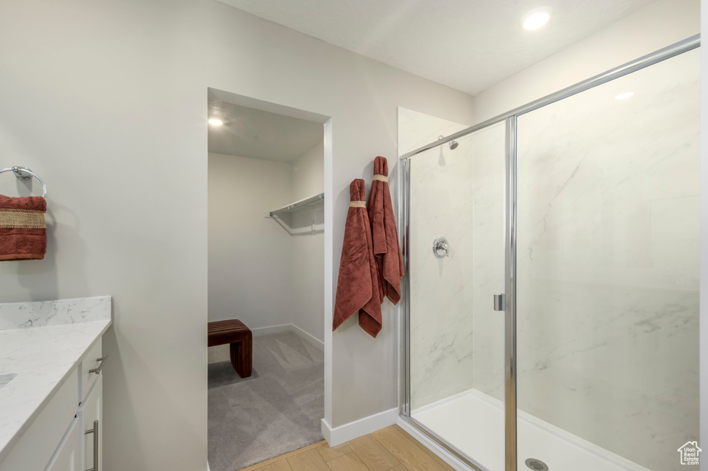 Bathroom with a marble finish shower, vanity, wood finished floors, and baseboards