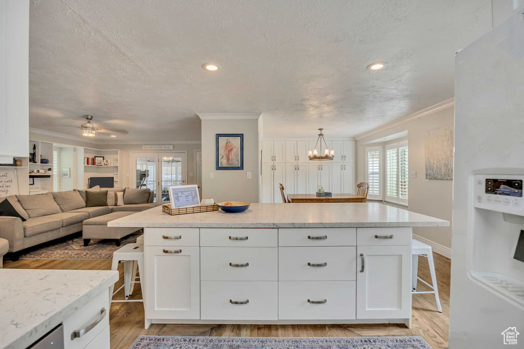Kitchen featuring ornamental molding, a breakfast bar area, light wood-style floors, white cabinets, and white refrigerator with ice dispenser