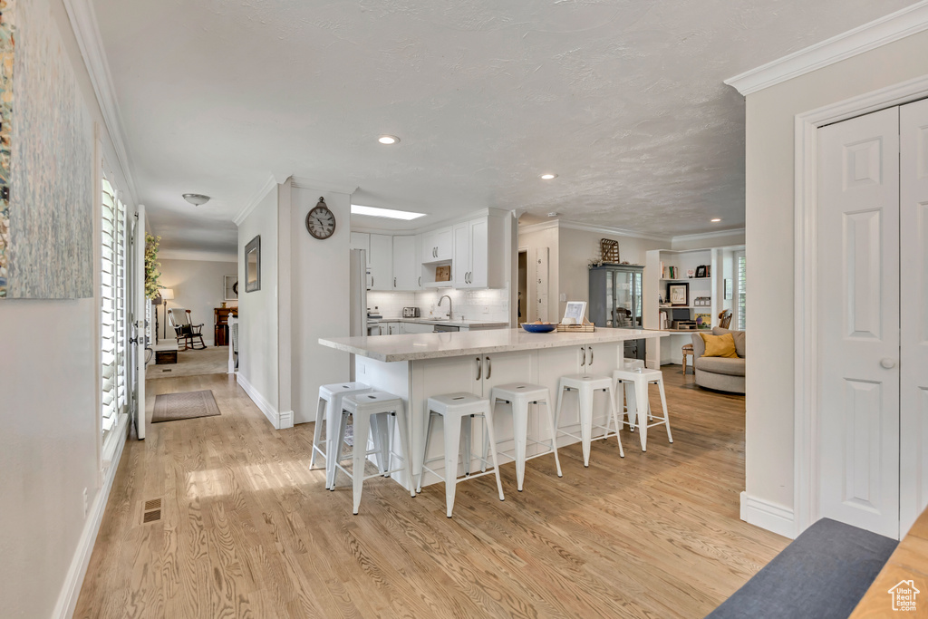 Kitchen with crown molding, a kitchen bar, light wood-style floors, white cabinetry, and baseboards