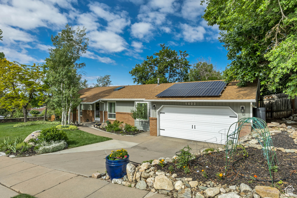 Single story home featuring brick siding, driveway, a garage, roof mounted solar panels, and a shingled roof
