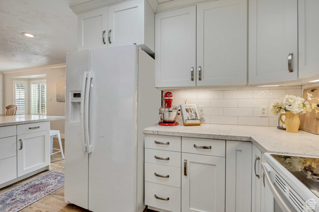 Kitchen with white fridge with ice dispenser, tasteful backsplash, light wood-style flooring, white cabinetry, and ornamental molding