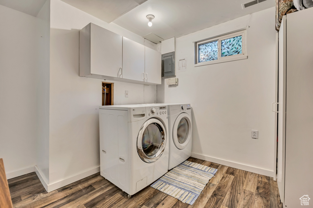 Washroom featuring cabinet space, washing machine and dryer, baseboards, electric panel, and wood finished floors