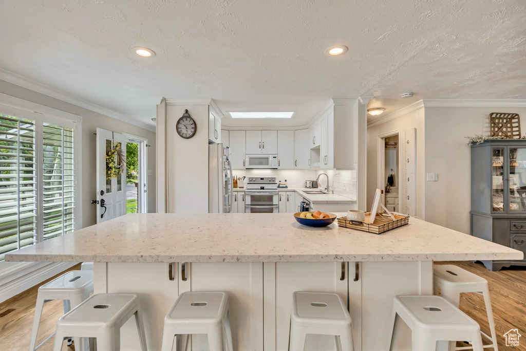 Kitchen with white appliances, light wood-style floors, light stone countertops, crown molding, and a textured ceiling