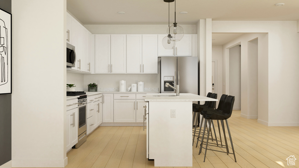Kitchen featuring stainless steel appliances, a center island with sink, light wood-style flooring, and a kitchen bar