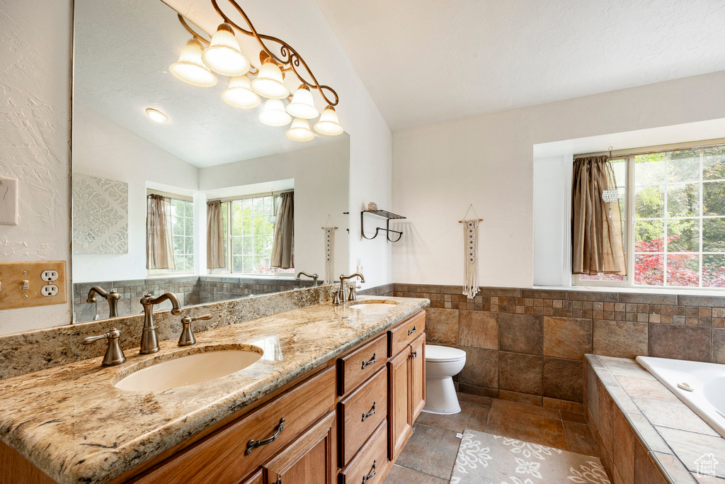 Full bathroom featuring vaulted ceiling, toilet, double vanity, tiled tub, and wainscoting