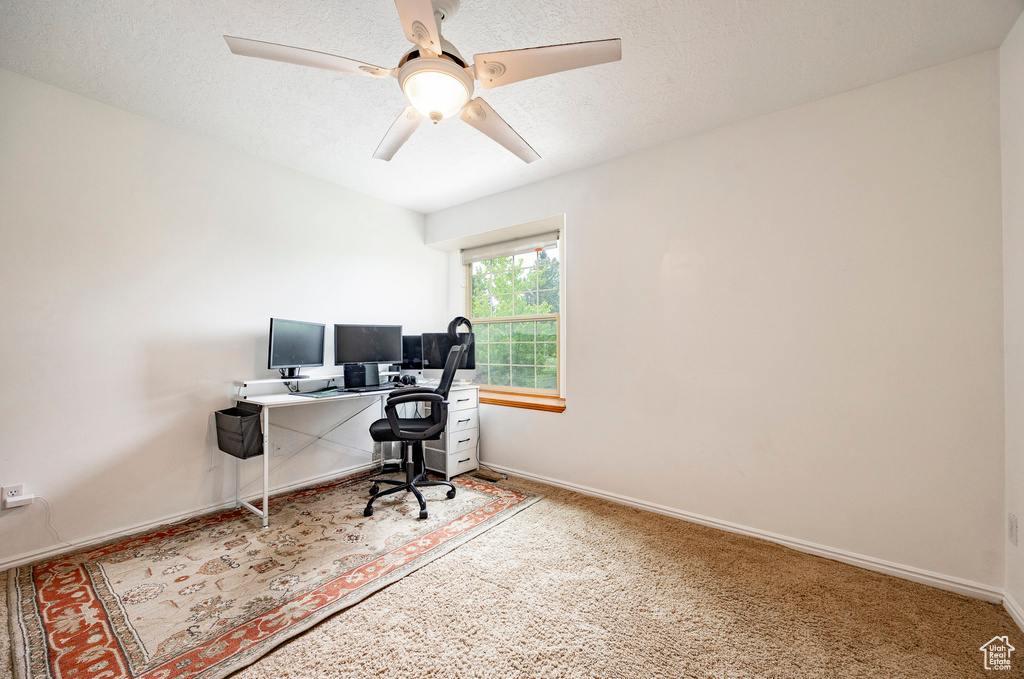 Carpeted home office featuring ceiling fan and baseboards