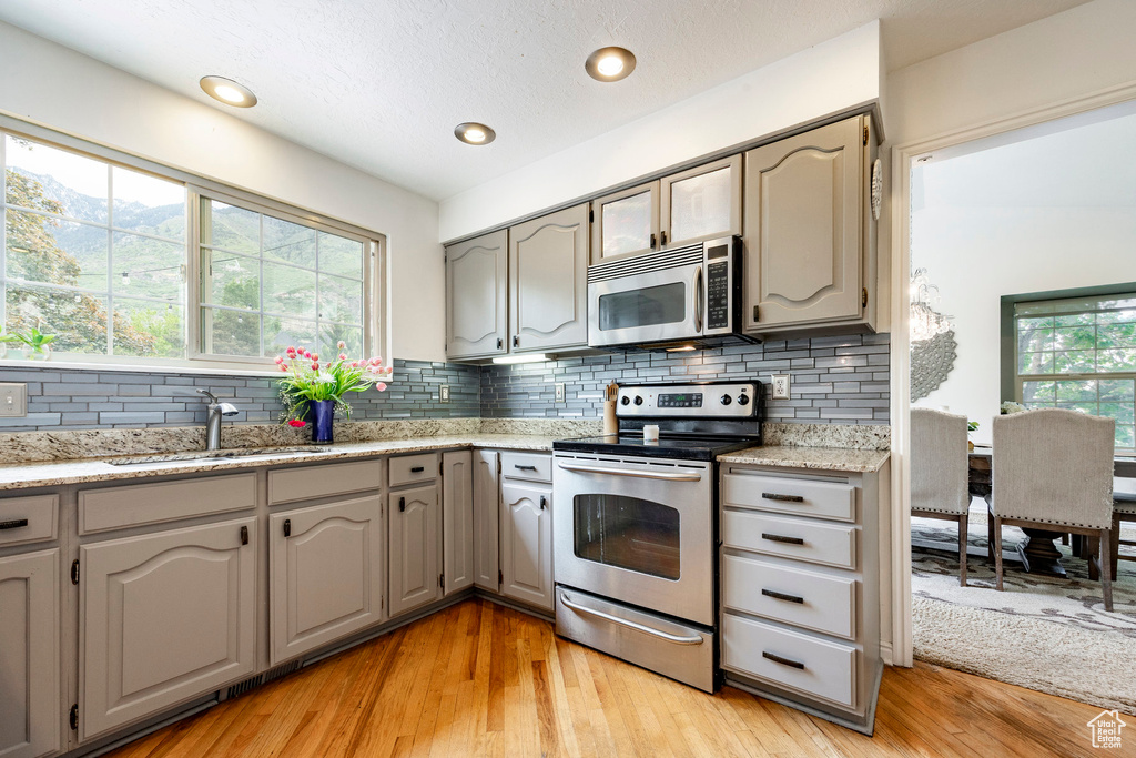 Kitchen with stainless steel appliances, a sink, backsplash, light wood-style flooring, and recessed lighting