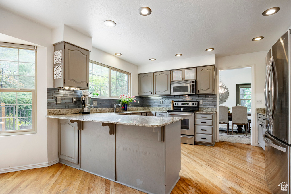 Kitchen featuring appliances with stainless steel finishes, a peninsula, a kitchen breakfast bar, light wood-type flooring, and recessed lighting