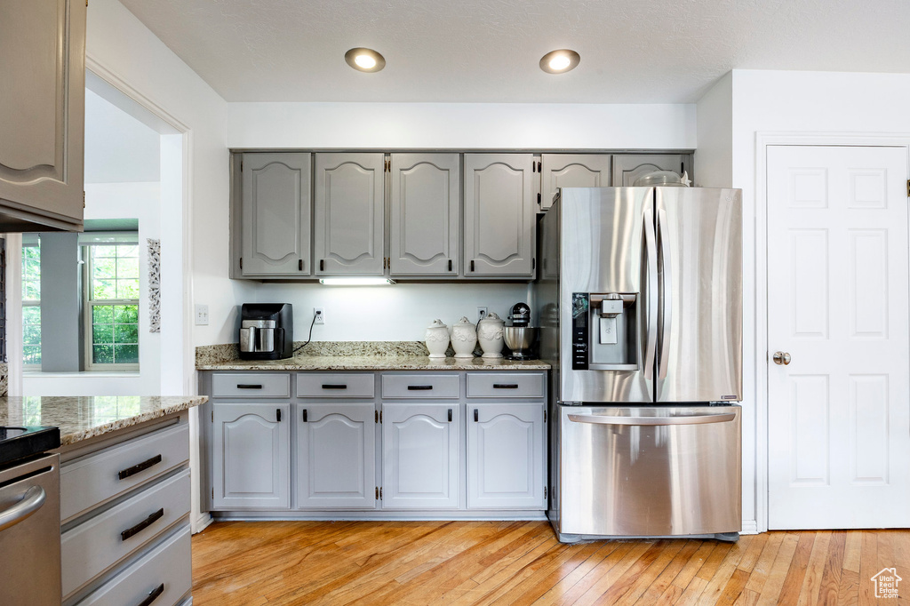Kitchen featuring stainless steel fridge, gray cabinets, light wood-type flooring, light stone counters, and stove