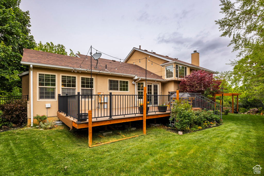 Back of house featuring stucco siding, a chimney, a wooden deck, and a yard