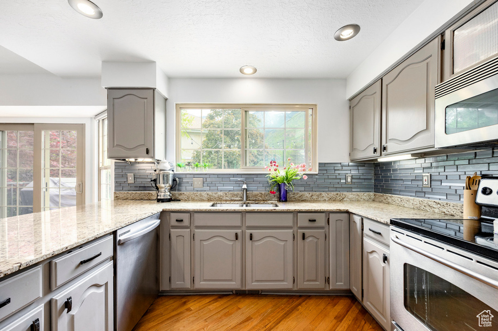 Kitchen with appliances with stainless steel finishes, a sink, gray cabinetry, backsplash, and light wood finished floors