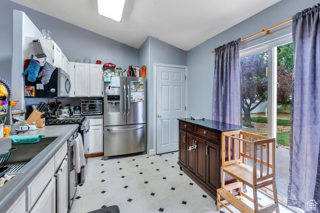 Kitchen featuring stainless steel appliances, light flooring, white cabinetry, lofted ceiling, and dark countertops