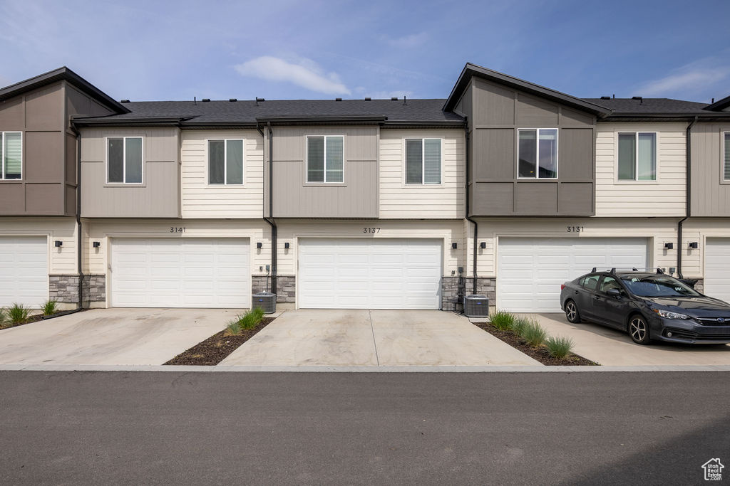 View of property featuring a garage, stone siding, driveway, and central AC
