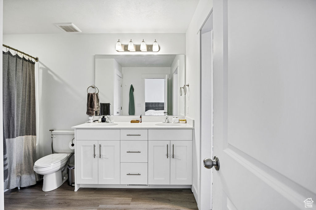 Full bathroom featuring wood finished floors, double vanity, toilet, and curtained shower