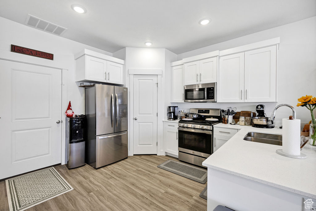 Kitchen featuring appliances with stainless steel finishes, a sink, light wood-style flooring, white cabinets, and recessed lighting
