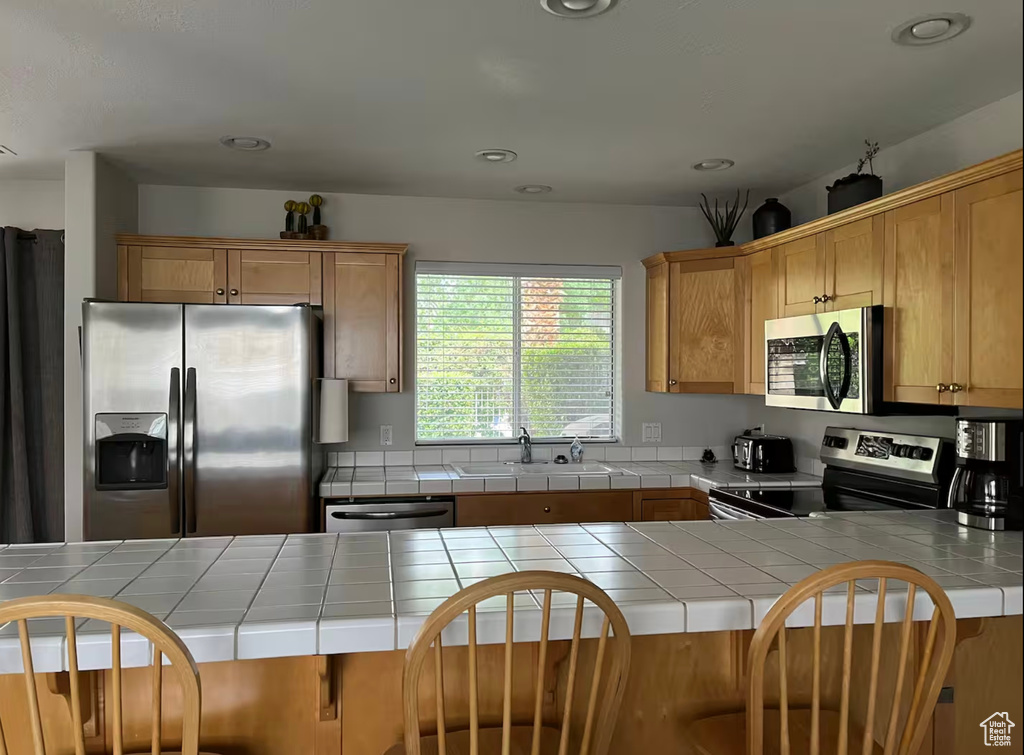 Kitchen with appliances with stainless steel finishes, tile counters, a sink, a peninsula, and recessed lighting