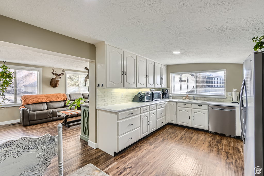 Kitchen with stainless steel appliances, dark wood-style flooring, healthy amount of natural light, white cabinets, and a textured ceiling