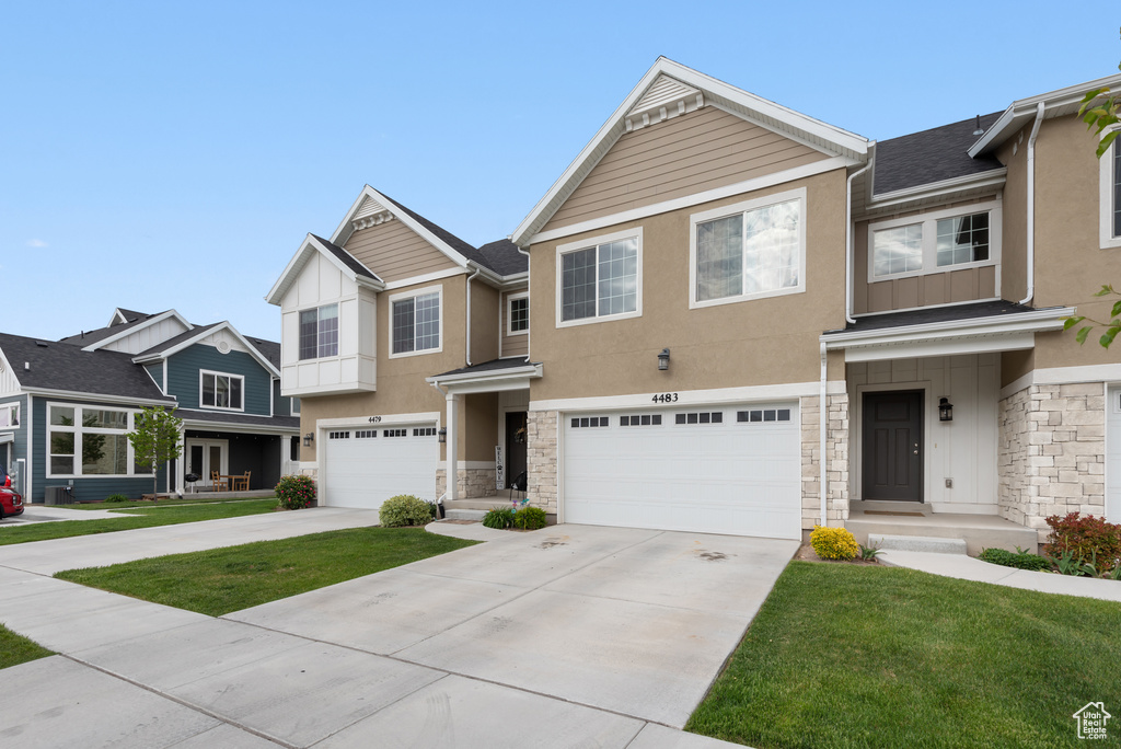 Multi unit property with stone siding, stucco siding, an attached garage, and driveway