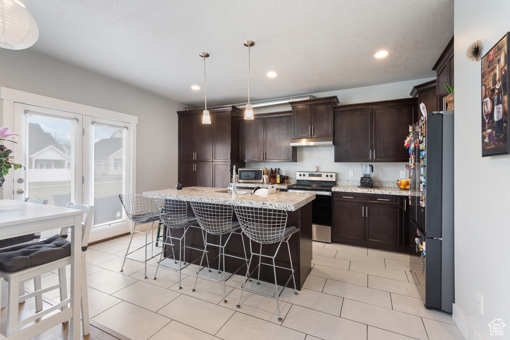 Kitchen featuring appliances with stainless steel finishes, under cabinet range hood, a kitchen breakfast bar, dark brown cabinets, and recessed lighting