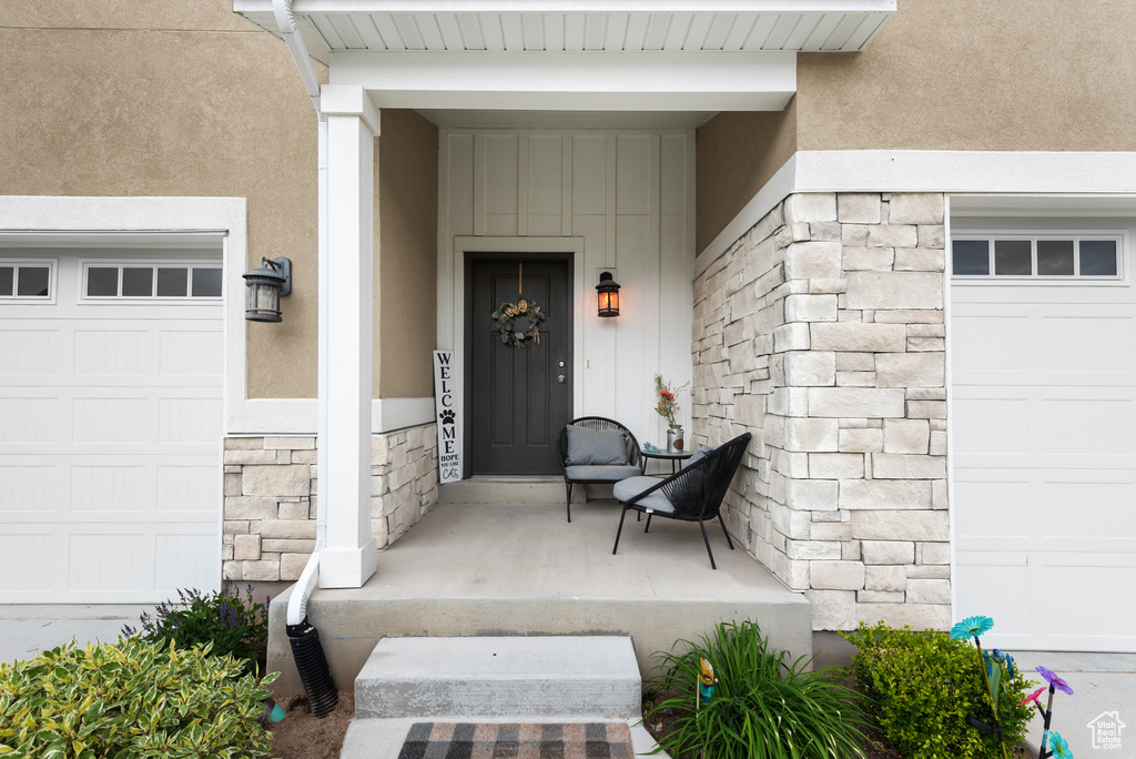 View of exterior entry featuring a garage, stone siding, stucco siding, and board and batten siding