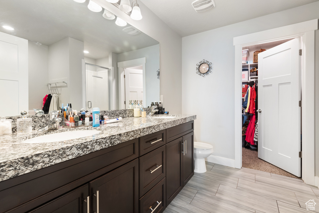 Full bathroom featuring a shower stall, double vanity, a spacious closet, toilet, and baseboards