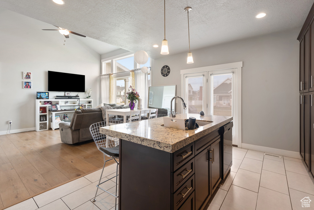 Kitchen with a sink, a breakfast bar area, a textured ceiling, open floor plan, and dishwasher