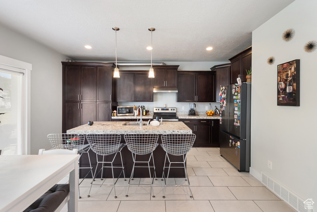 Kitchen featuring stainless steel appliances, a sink, dark brown cabinets, a breakfast bar, and recessed lighting